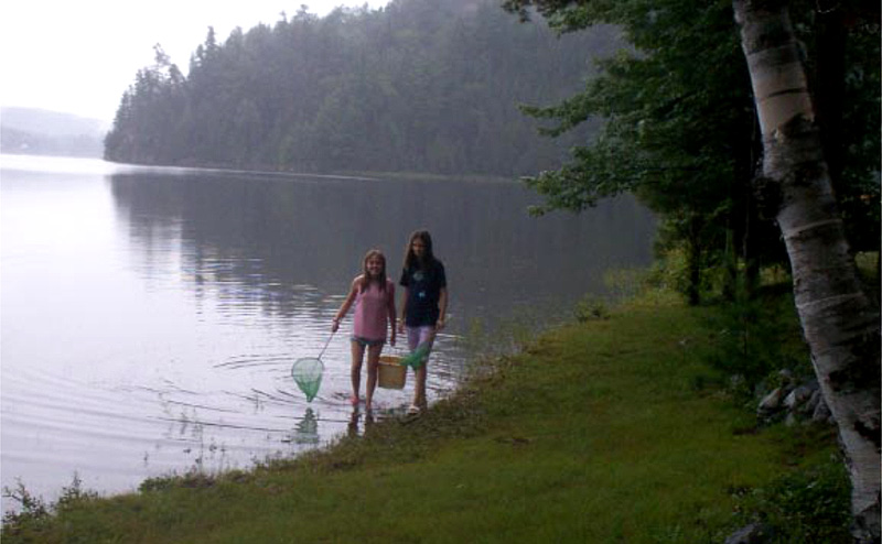 This is a photo of two young girls with a net and minnow pail trying to catch critters along the shore